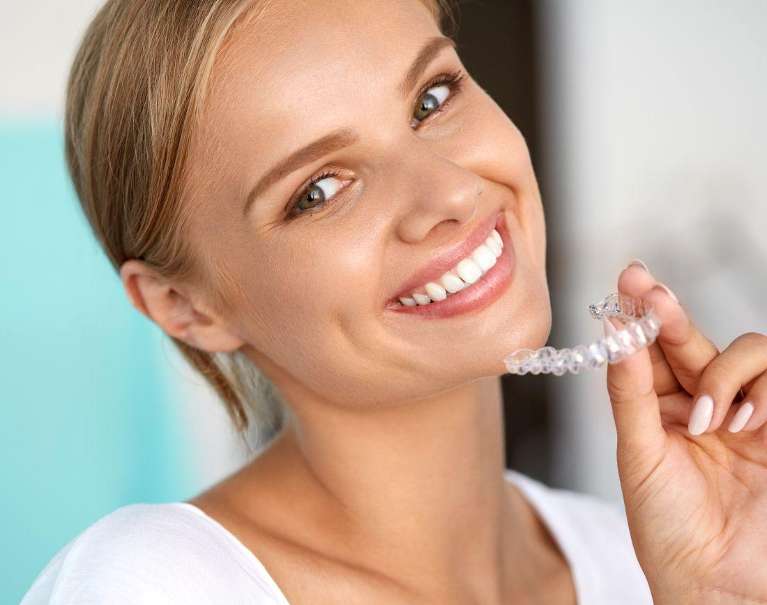 Smiling woman holding clear braces, showcasing confidence and a bright smile