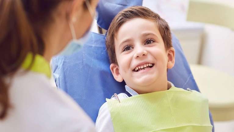 Smiling boy in dentist chair emphasizes the importance of regular dental visits for kids.